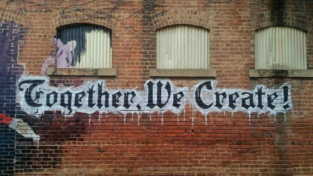 the side of a brick building with "together we create!" spray painted on the side.